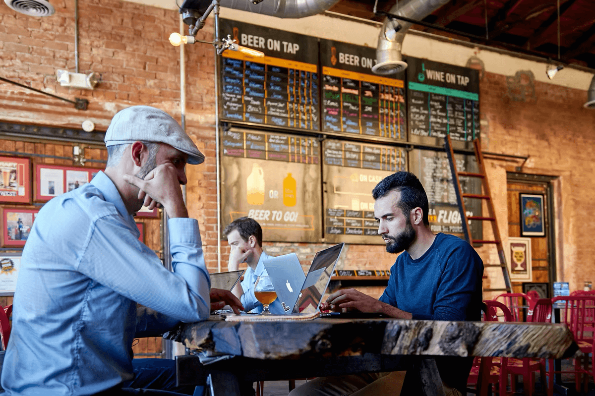 Des hommes travaillent sur leurs ordinateurs portables, installés dans un bar.