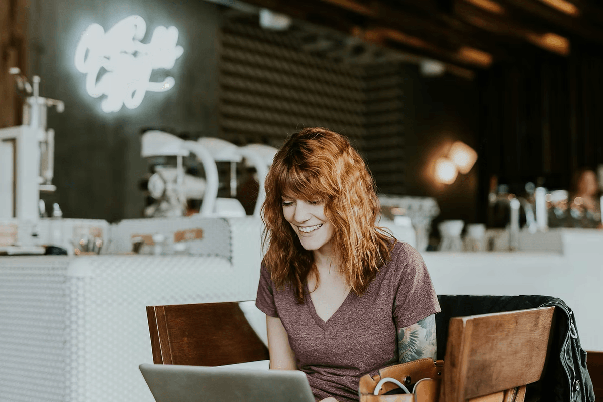 Une femme souriante utilise son ordinateur portable dans un café.